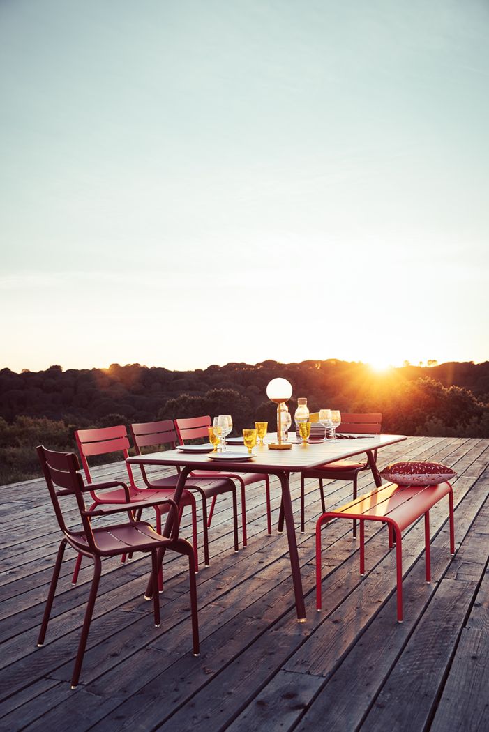 Luxembourg Tisch von Fermob im Outdoor-Bereich mit Stühlen und Bank bei Sonnenuntergang.