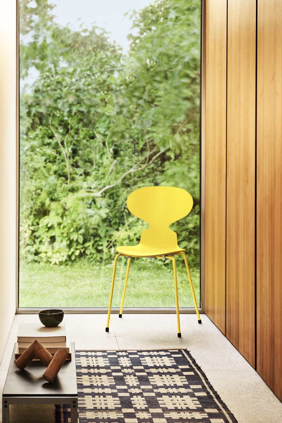 Gelber Fritz Hansen Stuhl vor Fenster mit Gartenblick, ergänzt durch Teppich und Tisch.
