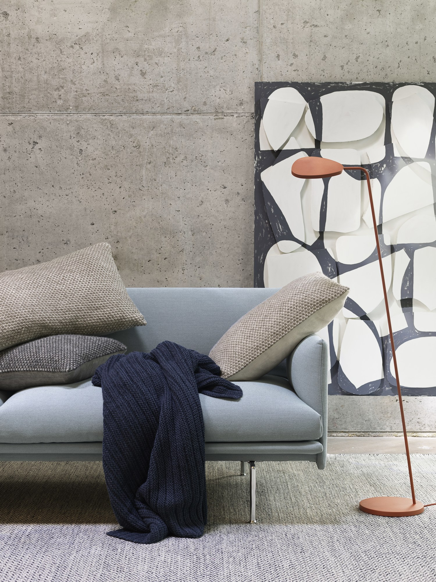 Nahaufnahme des Muuto Varjo Rug Teppichs in Grau, kombiniert mit Sofa, Kissen und Stehlampe.