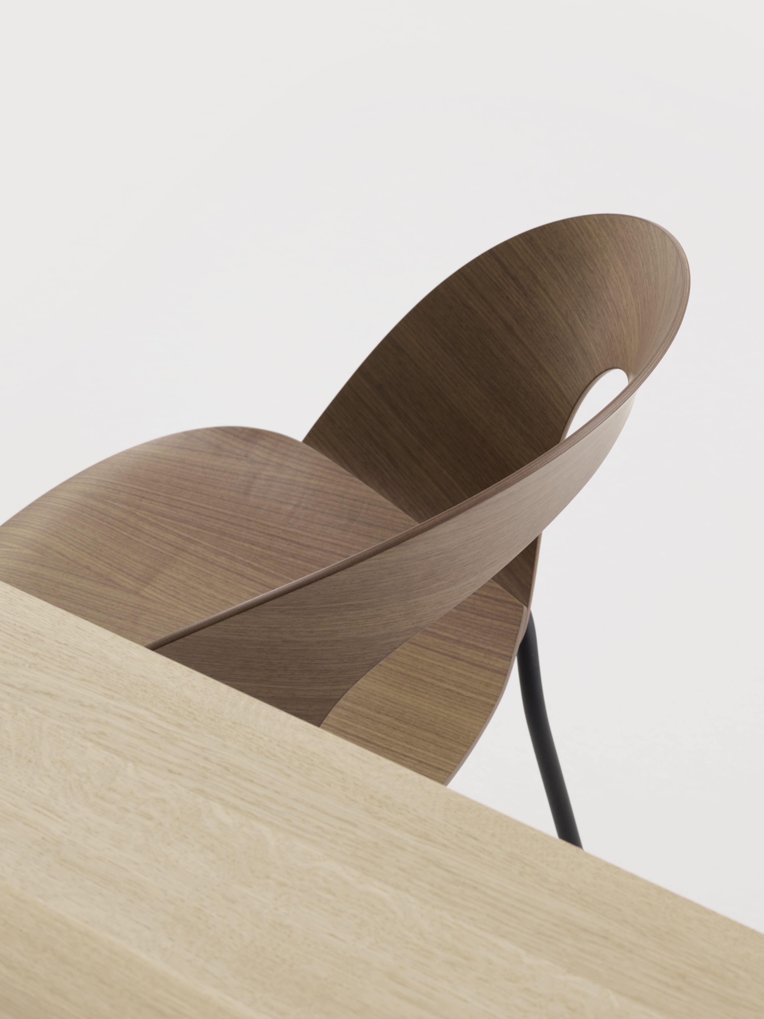 Detailaufnahme des Brunner Mudra Stuhls aus Holz mit schwarzem Metallgestell neben einem Holztisch.