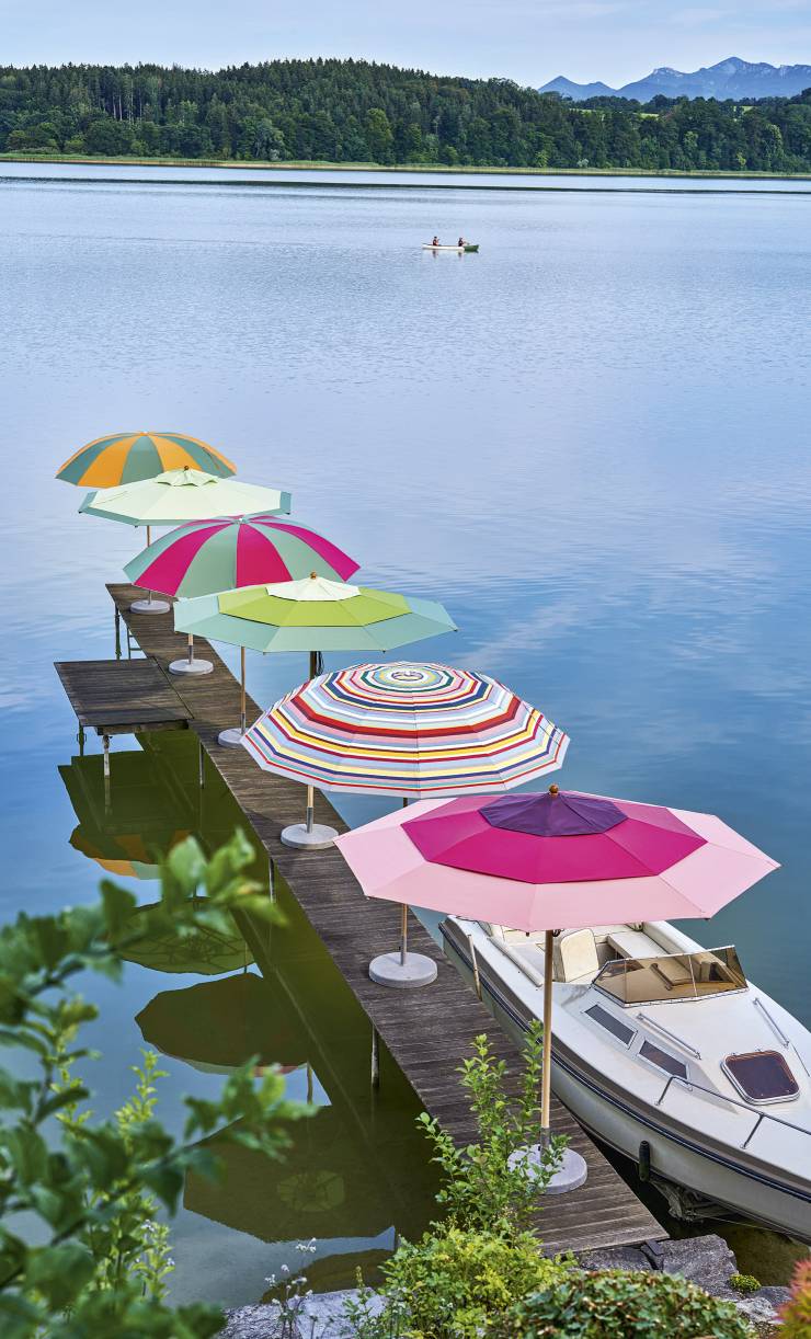 Mehrere farbenfrohe Weishäupl Pagodenschirme auf einem Holzsteg am See, ideal als Sonnenschutz für Garten und Terrasse.