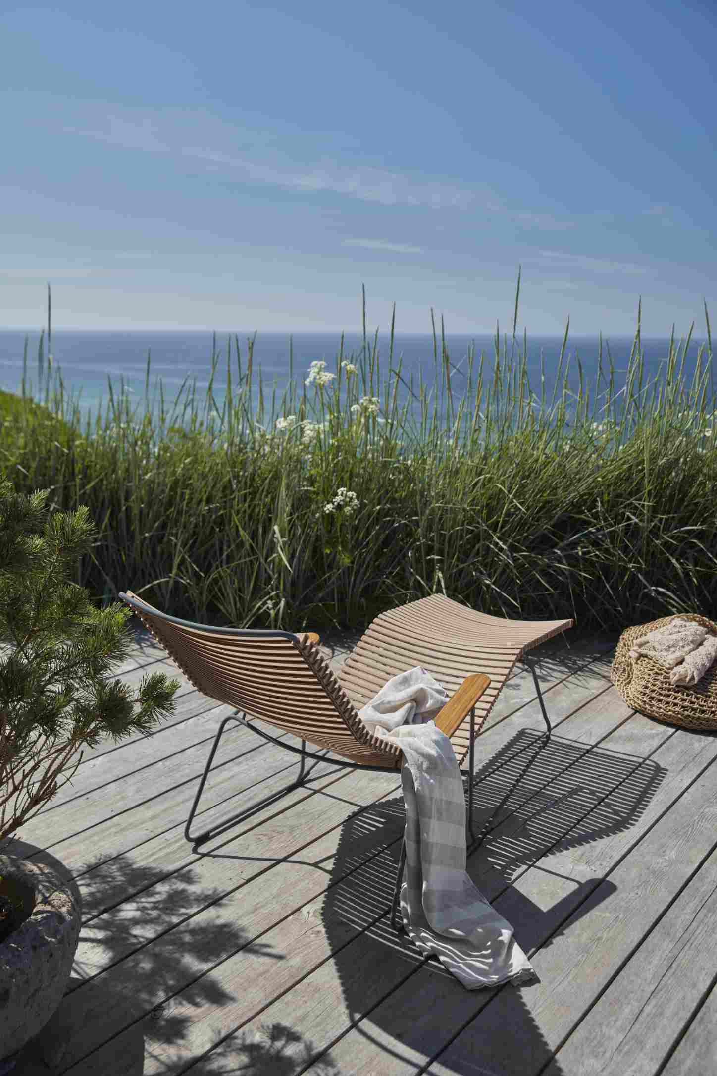 Click Sunrocker Sonnenliege von Houe: Dunkelgraue Outdoor Liege mit Decke auf Holzterrasse am Meer.