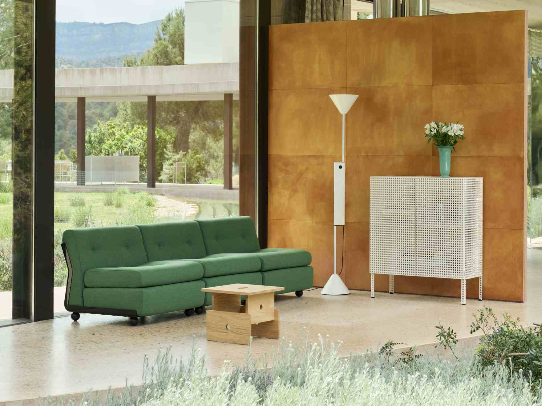 Helles Wohnzimmer mit Hay Sideboard "Perforated Cabinet Floor Medium", Stehlampe und grüner Couch.