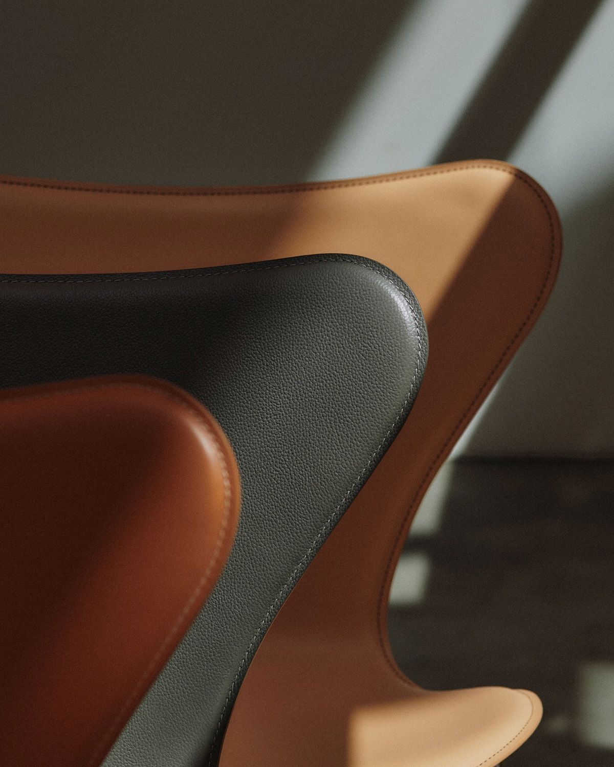 Detailaufnahme von drei Fritz Hansen Siebener Stühlen der Serie 3107 mit Lederbezug in Braun- und Grautönen.