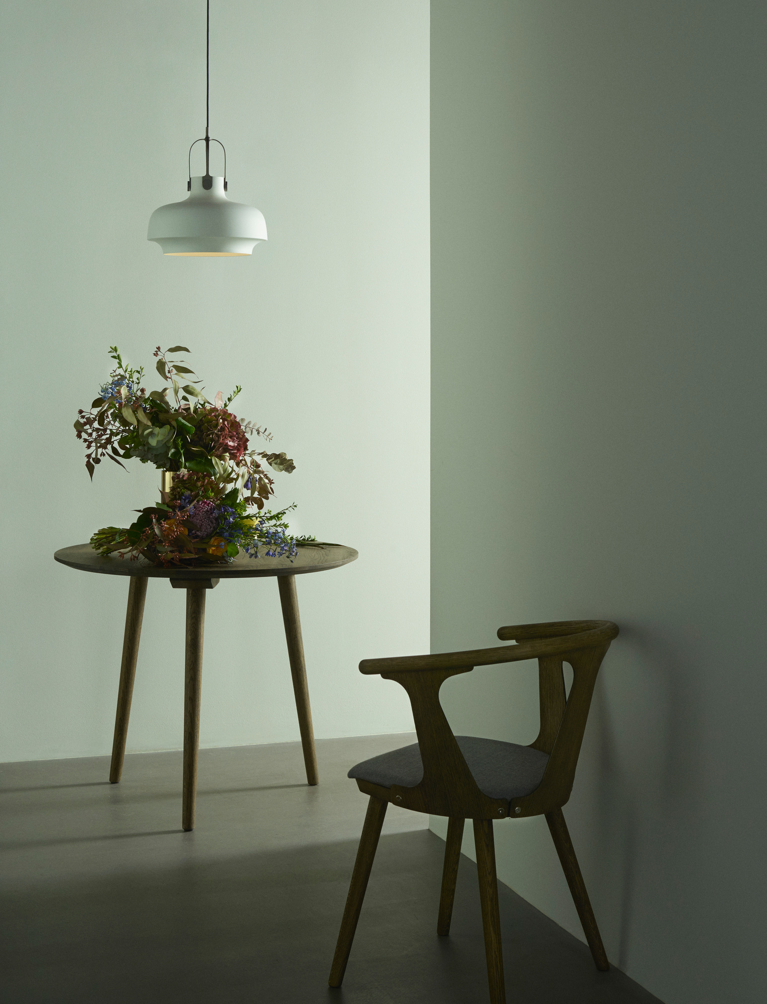 AndTradition In Between Chair SK1, schwarz lackierter Holzstuhl mit grauem Sitzpolster in minimalistischem Raum.