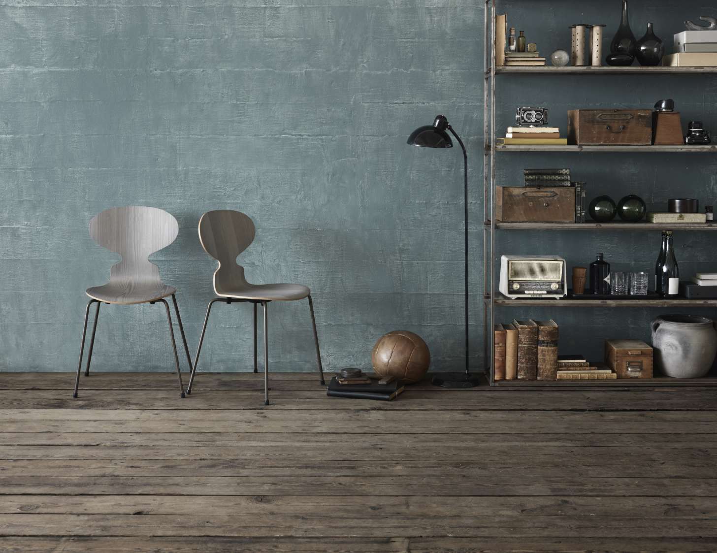 Zwei Fritz Hansen Ameise Stühle mit vierbeinigen Gestellen vor einer blauen Wand und Regal.