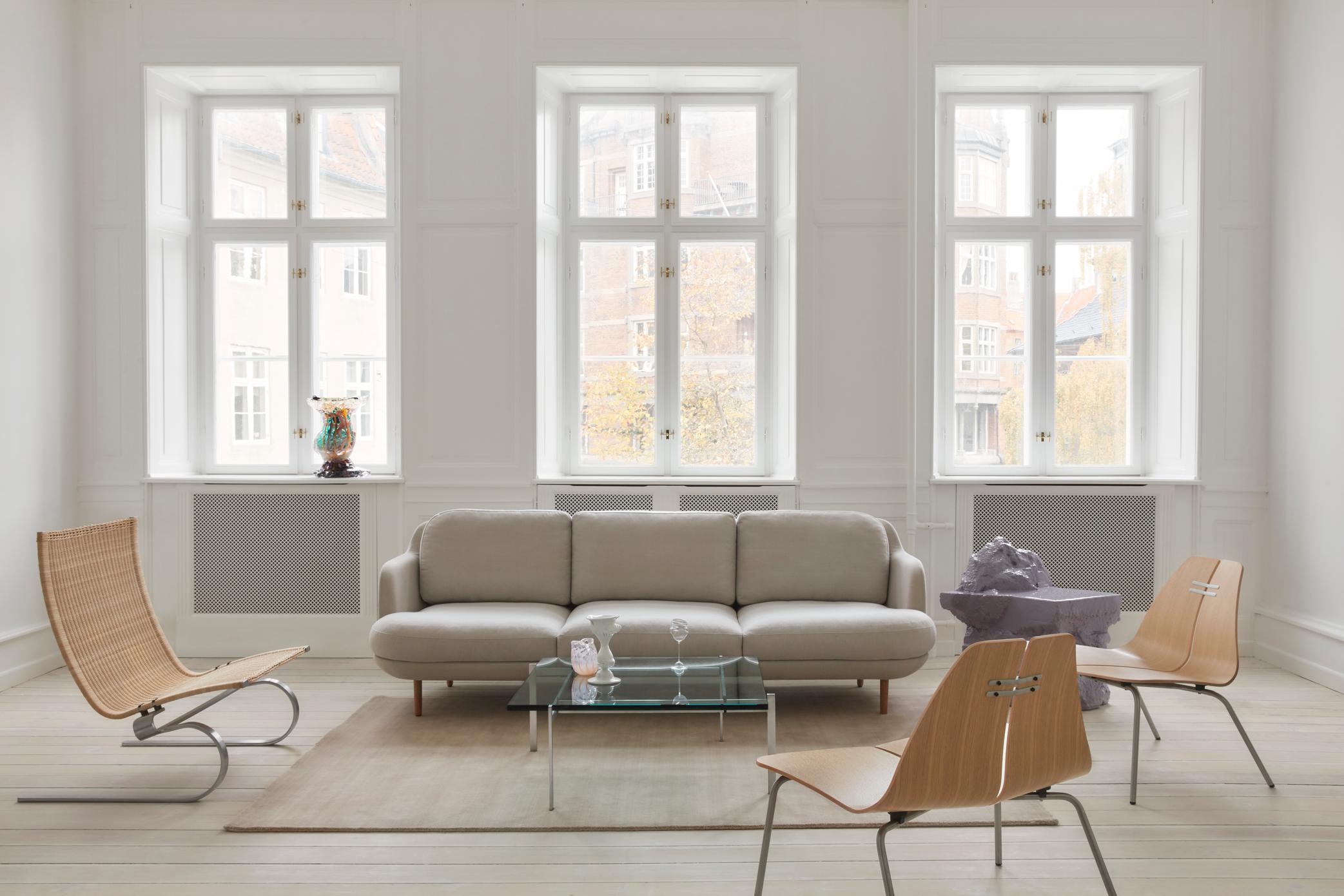 Heller Wohnraum mit PK23 Loungesessel von Fritz Hansen, Sofa, Glastisch und Design-Stühlen vor großen Fenstern.