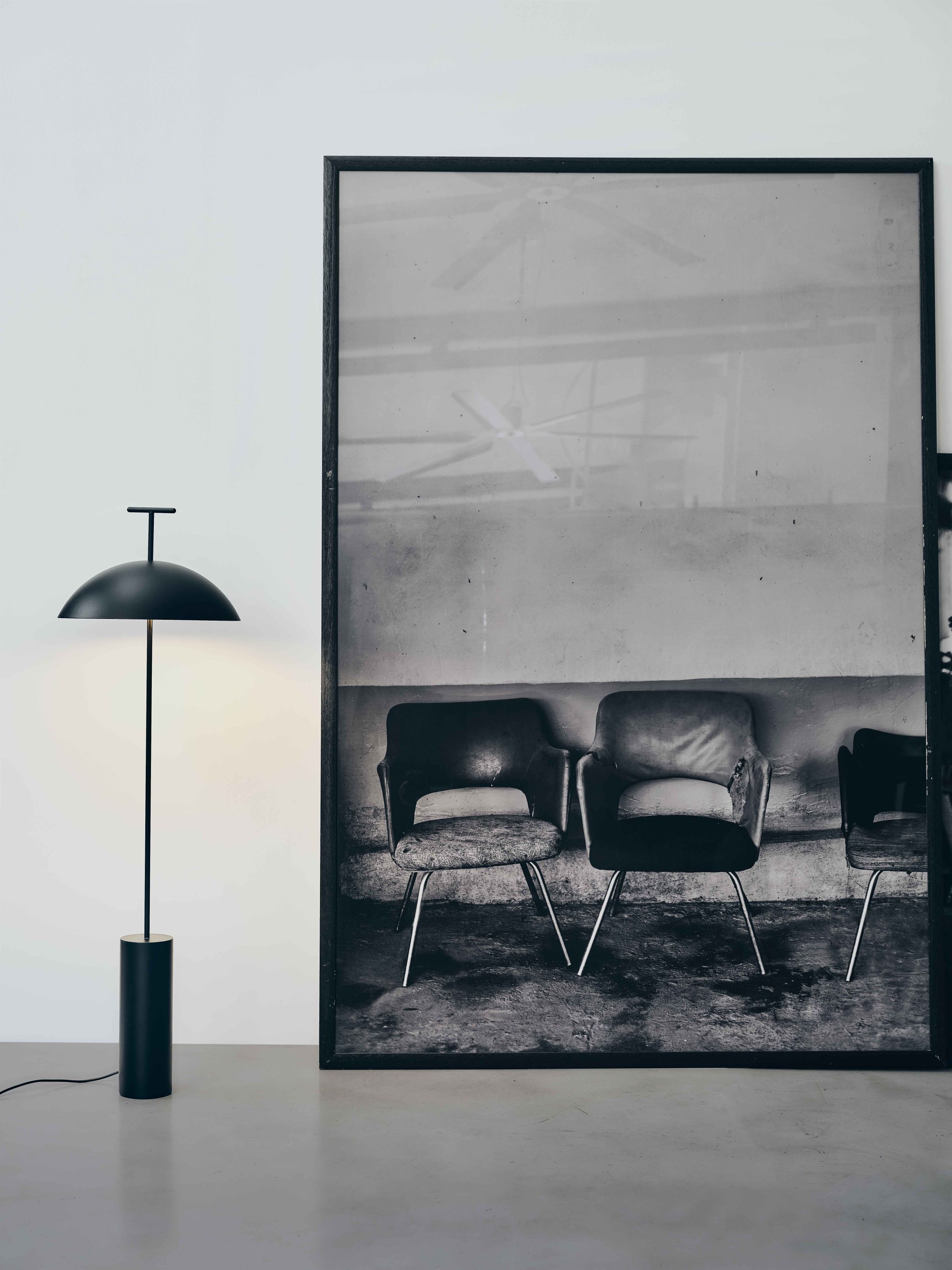 Minimalistische schwarze Stehleuchte neben einem gerahmten Schwarzweiß-Foto. Moderne Beleuchtung für Wohnzimmer.