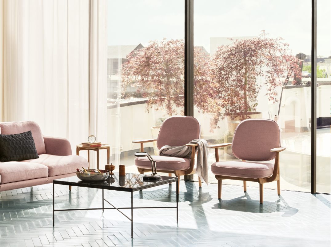 Heller Wohnraum mit Fritz Hansen Fred Loungesessel in Rosa, Sofa, Tisch und großem Fenster mit Baum.