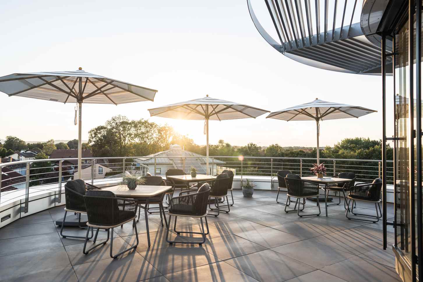 Weishäupl Klassiker Sonnenschirme auf einer Dachterrasse mit Tischen und Stühlen bei Sonnenuntergang.