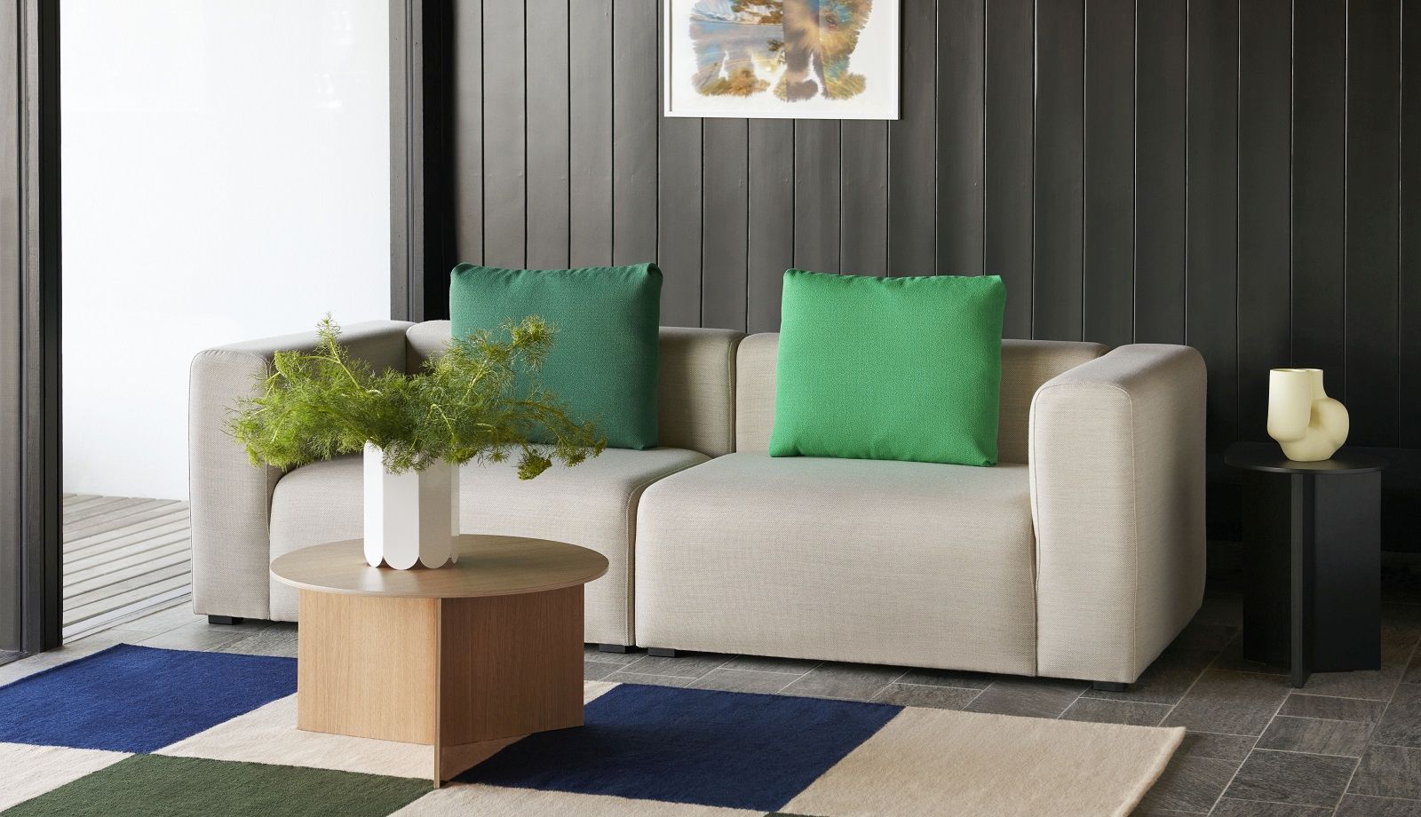 Hay Slit Table Wood Round XL Beistelltisch aus Eiche neben beigem Sofa mit grünen Kissen.