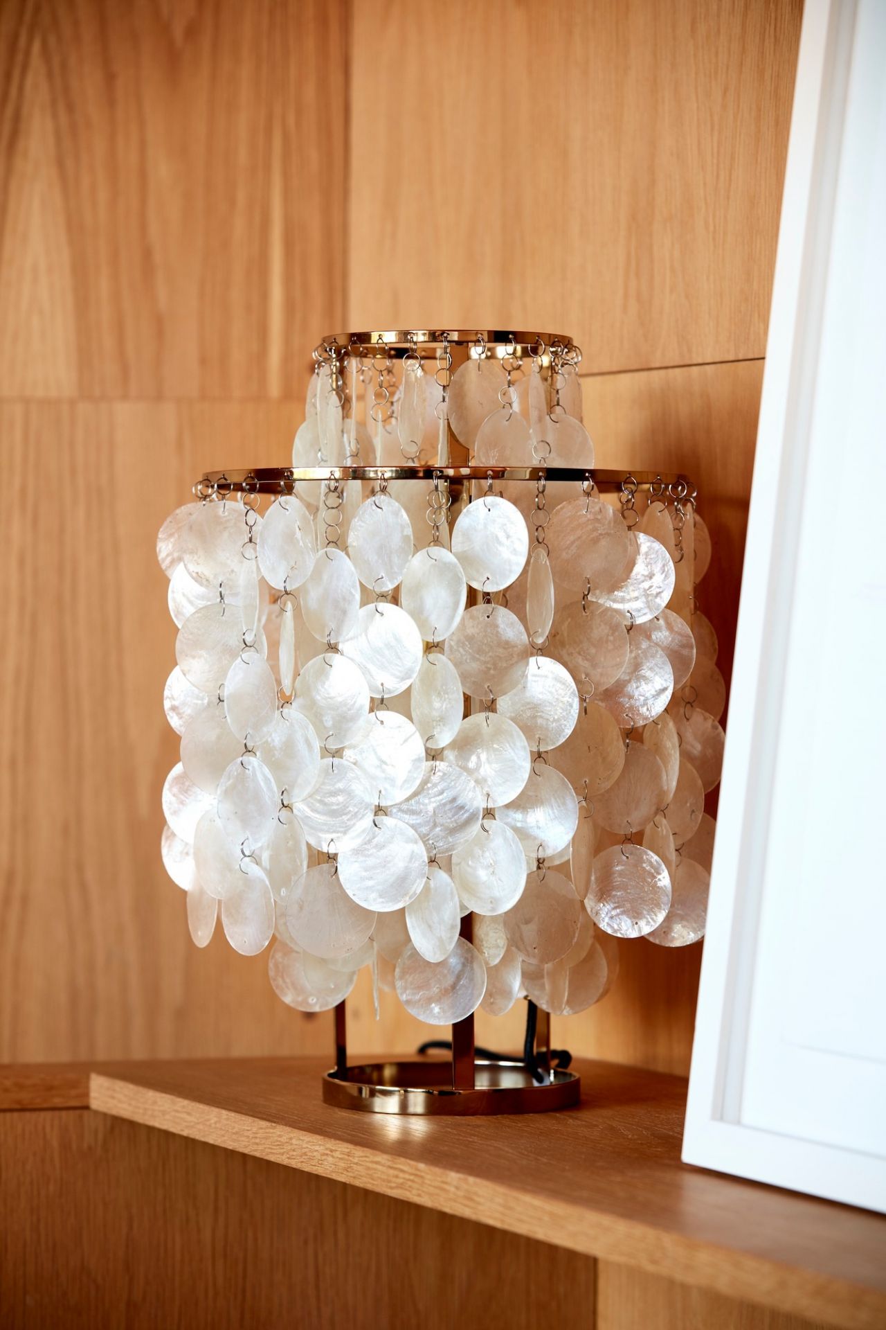 Elegante Tischleuchte mit goldenem Gestell und Lampenschirm aus schimmernden, weißen Muschelscheiben für stilvolle Beleuchtung.