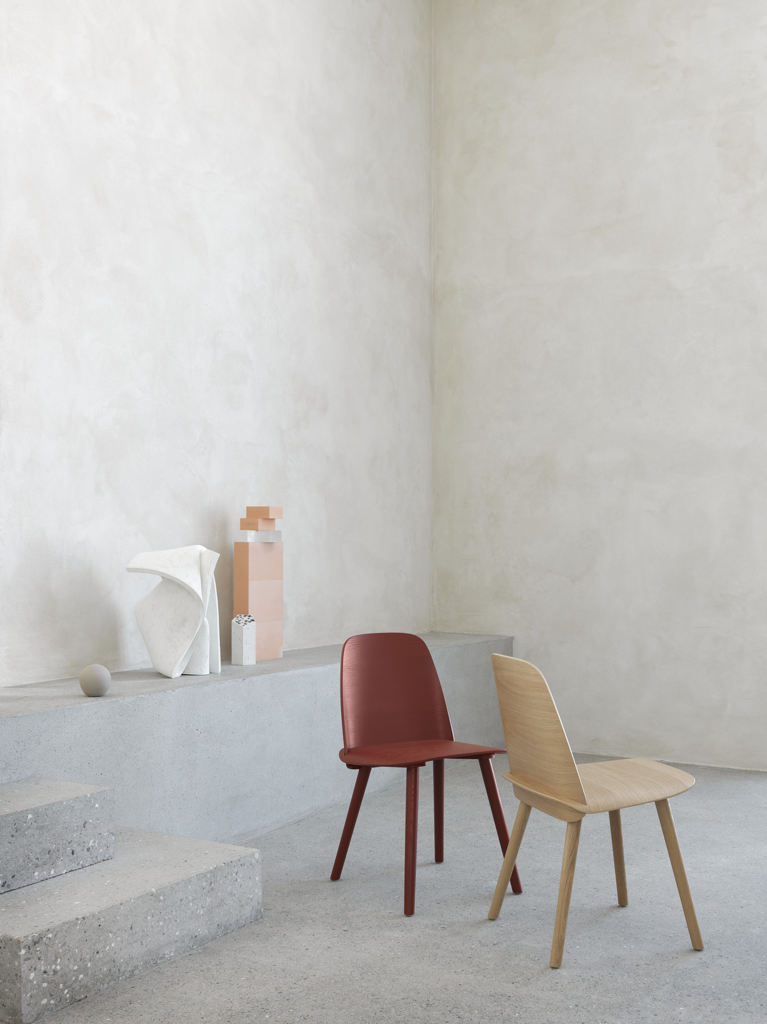 Zwei Muuto Nerd Chairs: ein Holzstuhl und ein rotbrauner Stuhl im minimalistischen Interieur.
