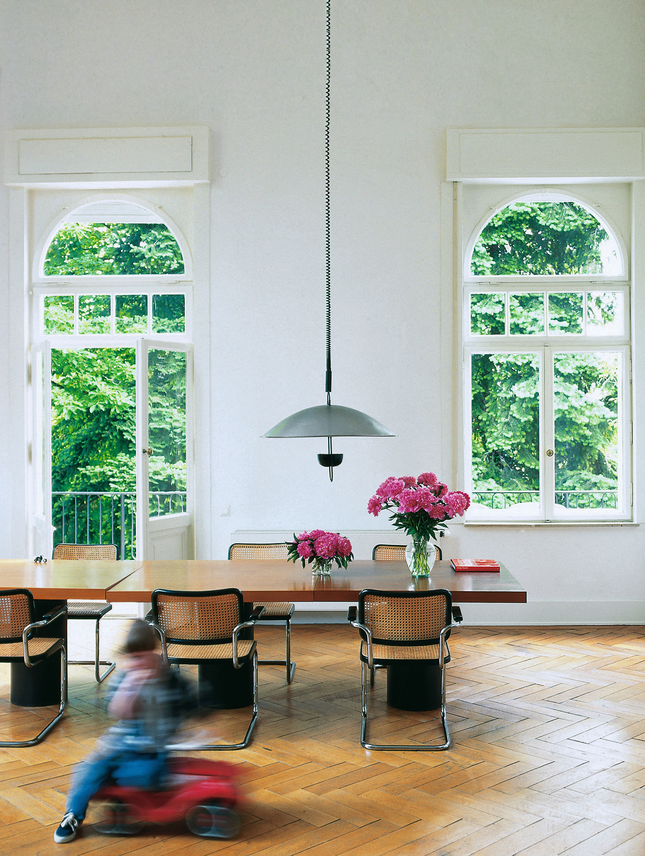 Esszimmer mit Thonet S 64 Freischwinger Stühlen in Schwarz und Chrom, langer Holztisch und Parkettboden.