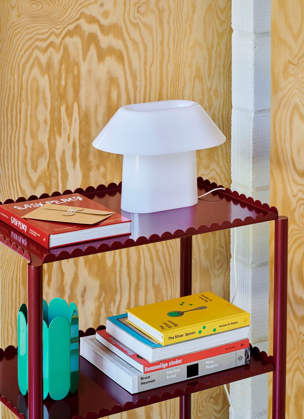 Weiße Drome Tischleuchte von Hay auf einem roten Regal mit Büchern, Nahaufnahme, modernes Design.