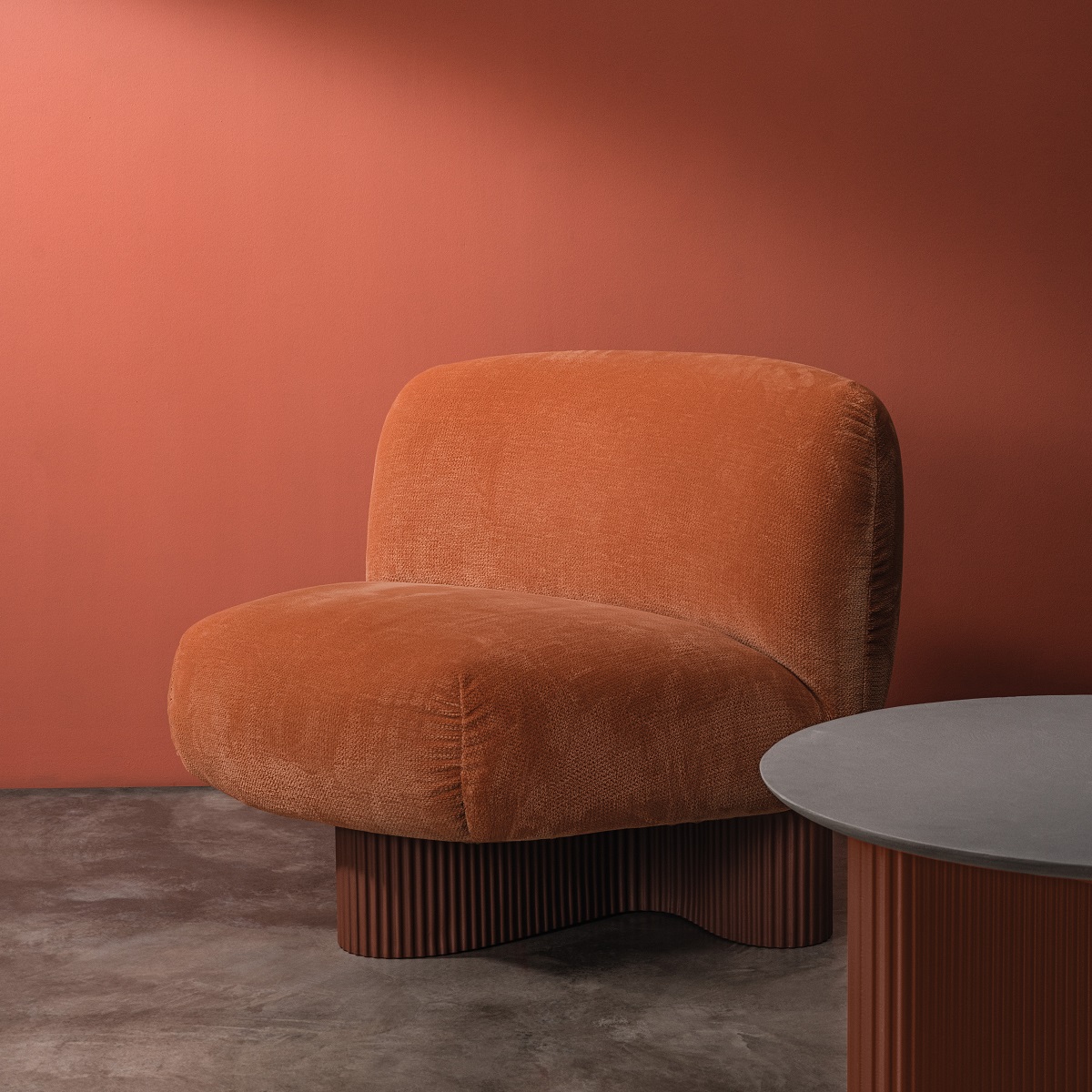 Bolete Lounge Sessel in Orange mit geriffeltem Sockel und passendem Beistelltisch vor farbiger Wand.
