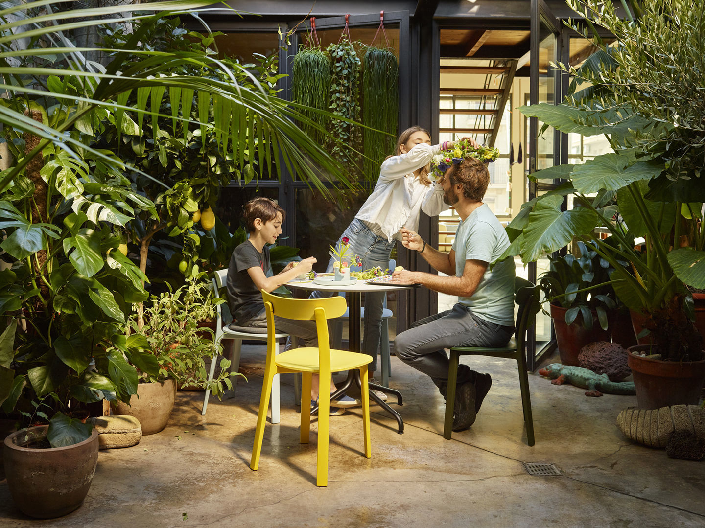 Familie sitzt im Garten auf Vitra All Plastic Chairs in Gelb und Grün beim Basteln.