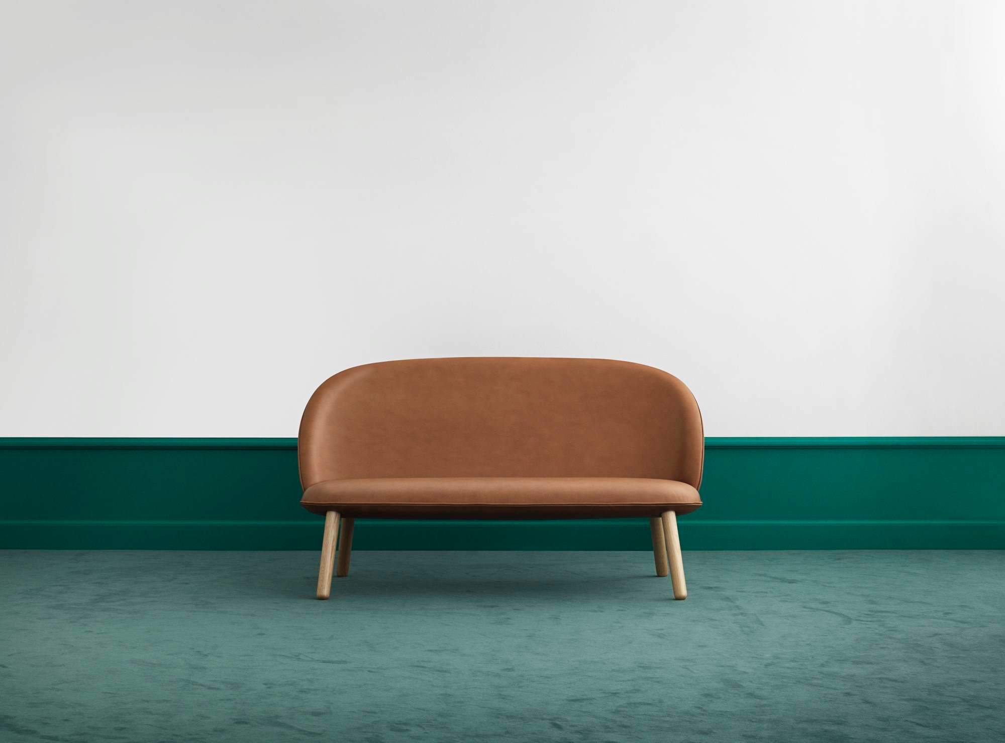 Ace Sofa von Normann Copenhagen in Brandy-Leder mit Holzbeinen vor grüner Wand.