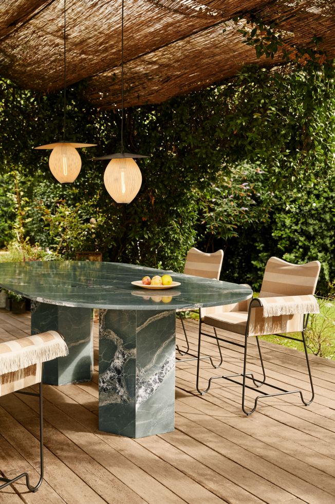 Gubi Epic Outdoor Esstisch Ellipse aus grünem Marmor mit Stühlen und Lampen im Garten.