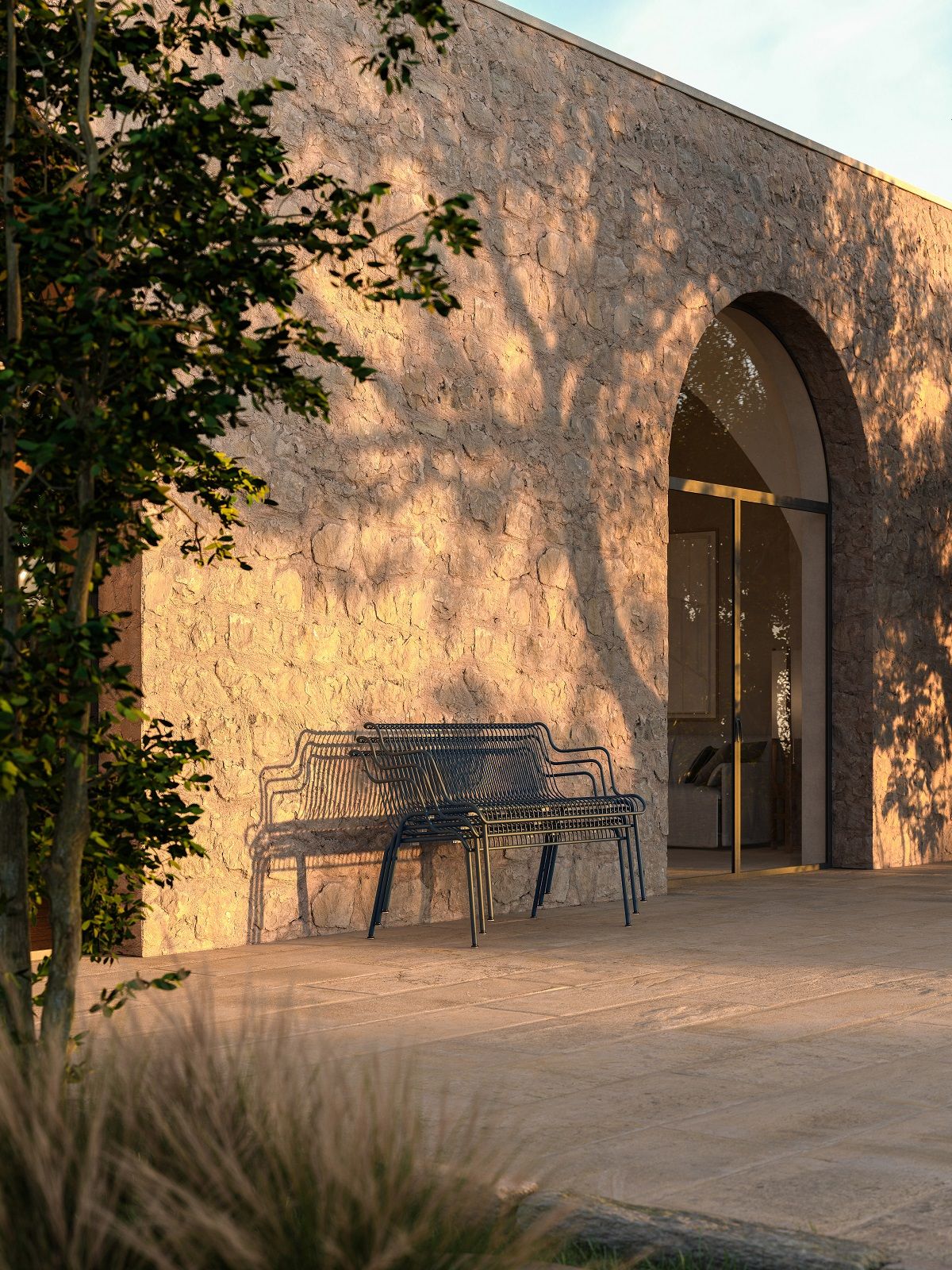 South Outdoor Bank von Magis vor einer Steinwand mit Baumschatten, moderne Gartenbank.