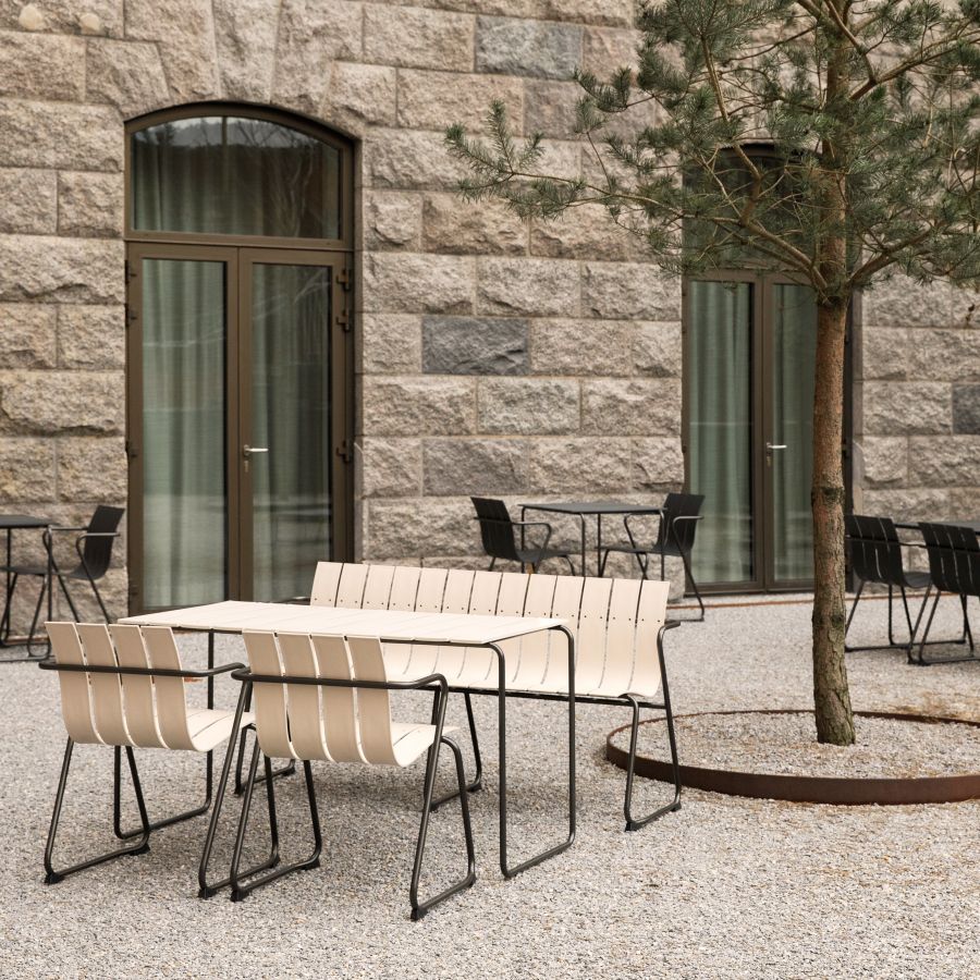 Beige Gartenmöbel-Set mit Tisch, Bank und Stühlen auf Kies vor einer Steinwand.