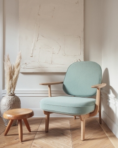 Heller Fritz Hansen Sessel Fred mit mintgrünem Bezug und Holzgestell neben kleinem Hocker.