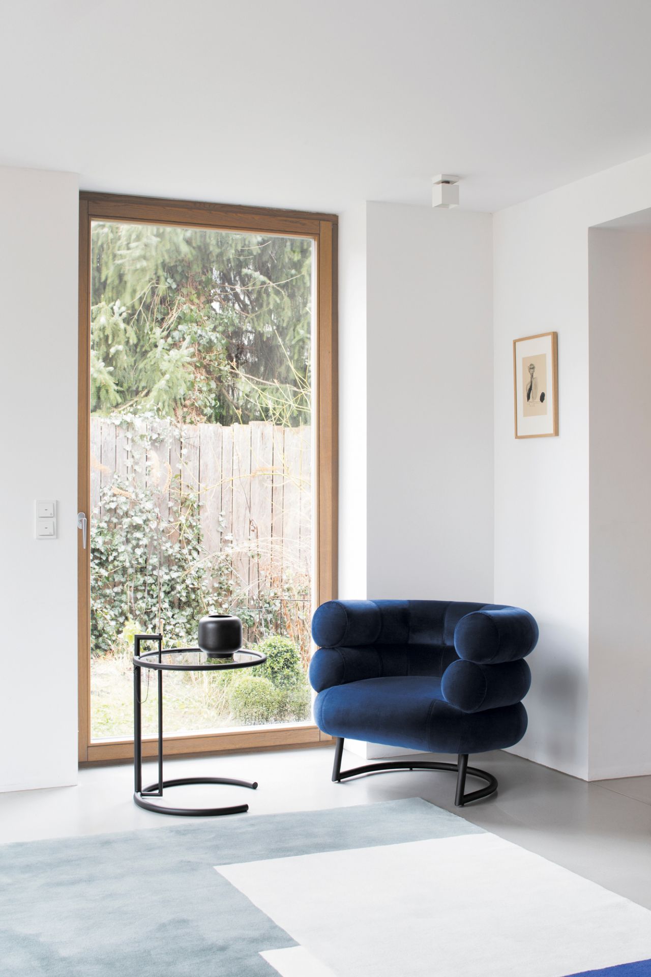 Blauer Samtsessel mit rundem Beistelltisch und schwarzer Vase in modernem Wohnzimmer mit Fenster.