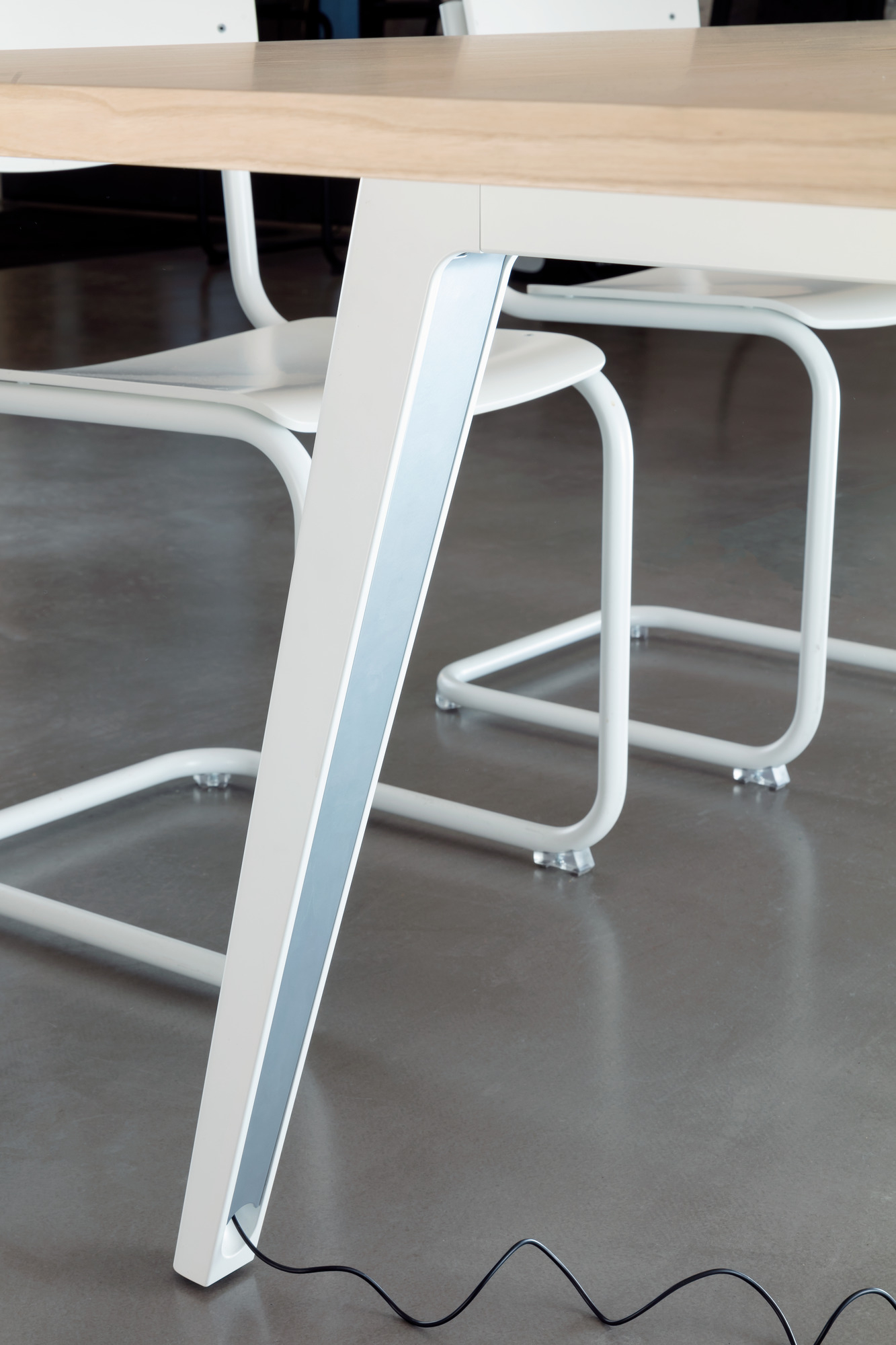 Detailaufnahme vom Bein des Thonet 1500 Tisches mit weißem Gestell und hellem Holztischblatt, Kabel am Boden.