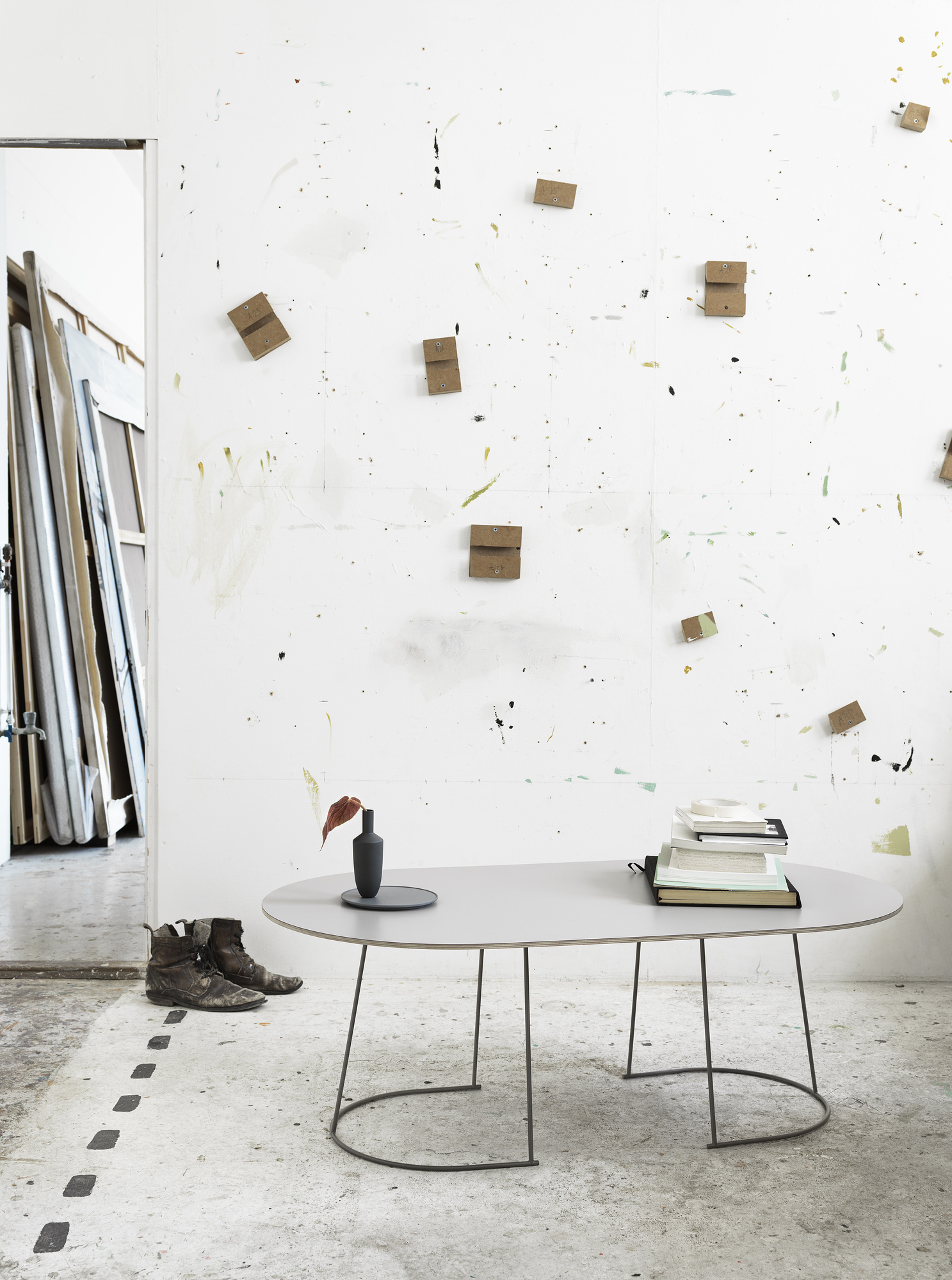 Muuto Airy Coffee Table Large: Ovaler Couchtisch in Grau mit filigranem Metallgestell in einem Atelier.
