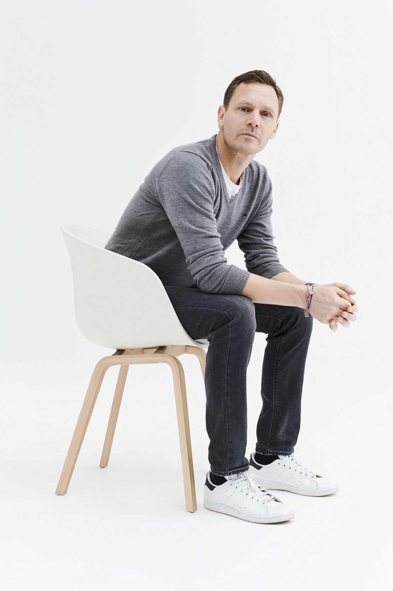 Mann sitzt auf einem weißen About a Chair AAC213 Stuhl von Hay mit Holzbeinen.