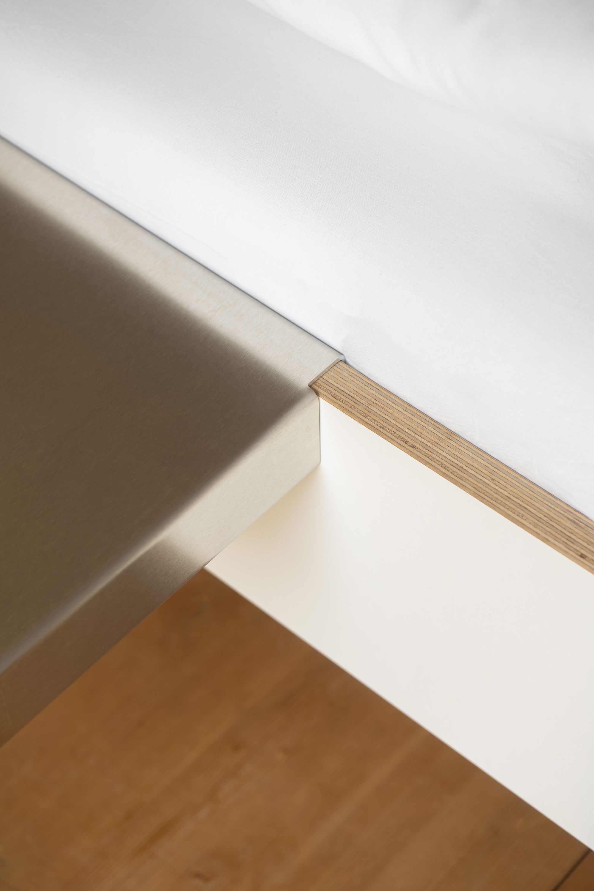 Detailaufnahme der Moormann Bettkante Leicht Seitenablage aus Metall und Holz am weißen Bett für Schlafzimmer.