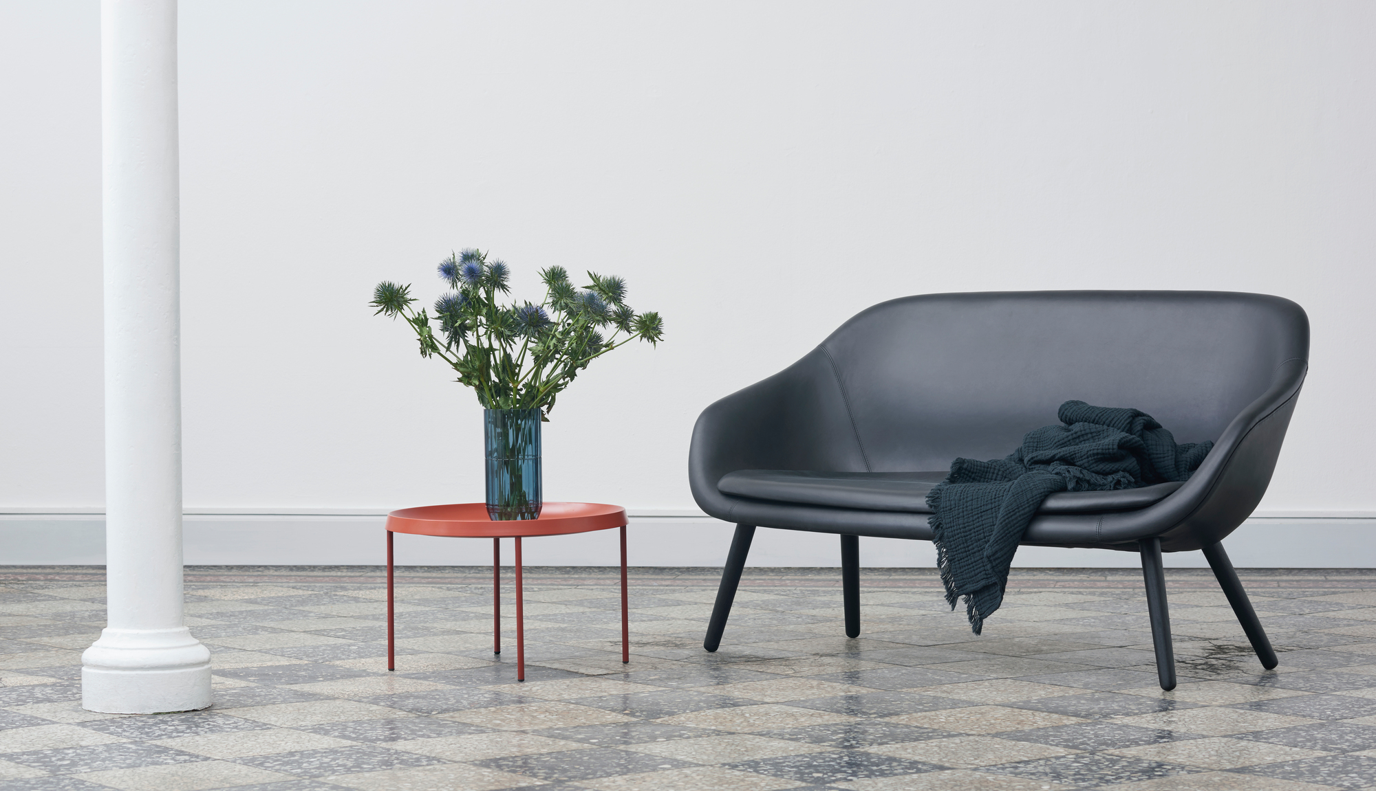 Schwarzes About a Lounge Sofa von Hay mit Decke und Beistelltisch mit Blumen in minimalistischem Raum.
