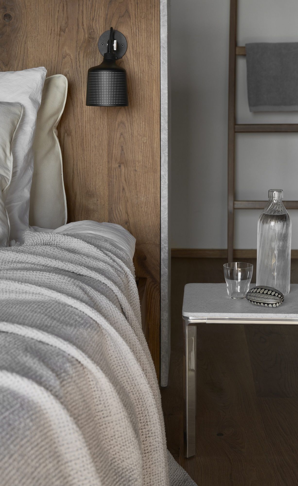 Nahaufnahme eines Vipp Nachttisches mit Wasserflasche und Glas neben einem Bett.