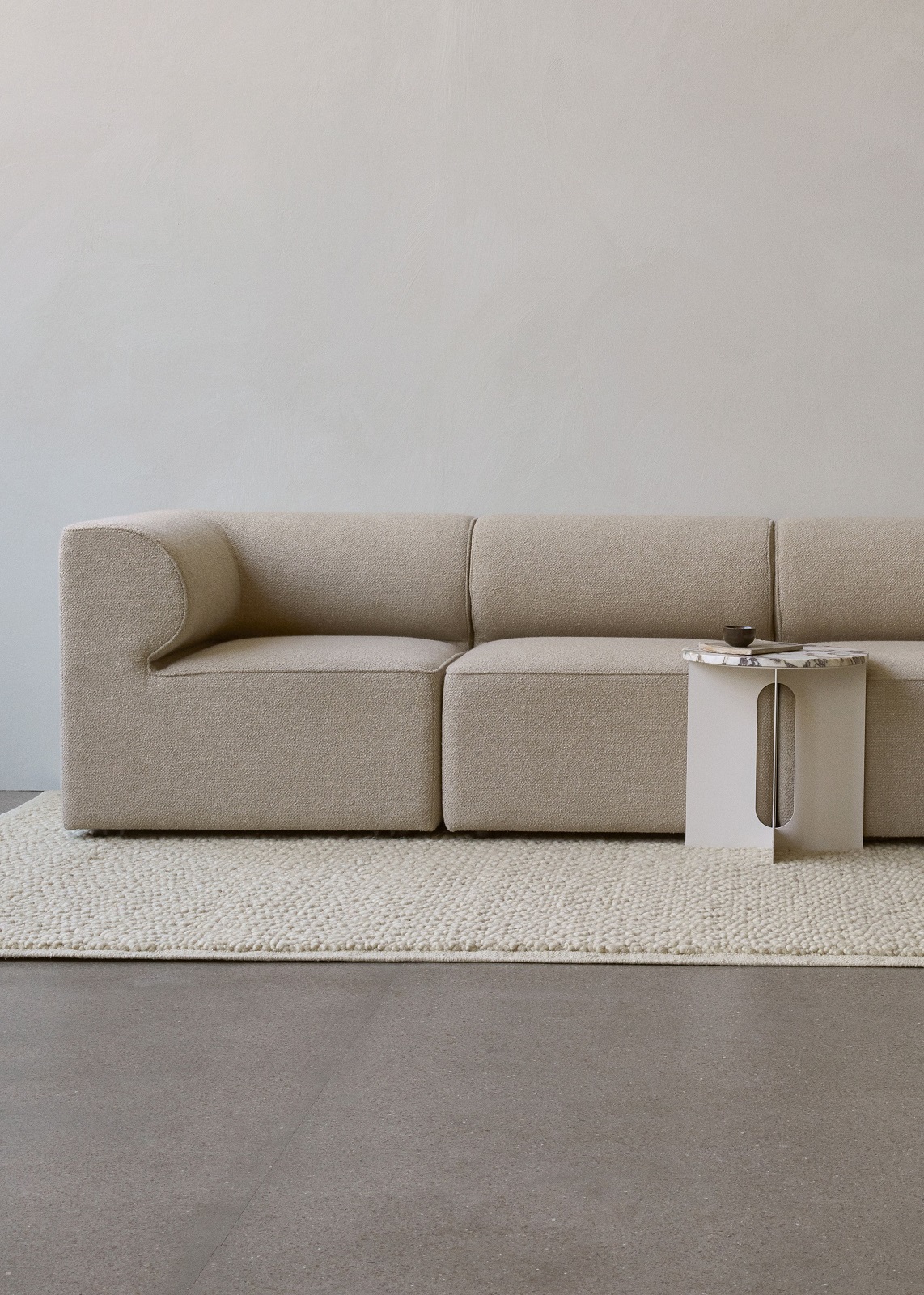 Audo Copenhagen Gravel Rug Teppich in Beige unter einem modularen Sofa und Beistelltisch.