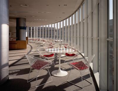 Innenaufnahme mit Knoll International Diamond Sesseln mit roten Sitzkissen an runden Tischen in modernem Gebäude.