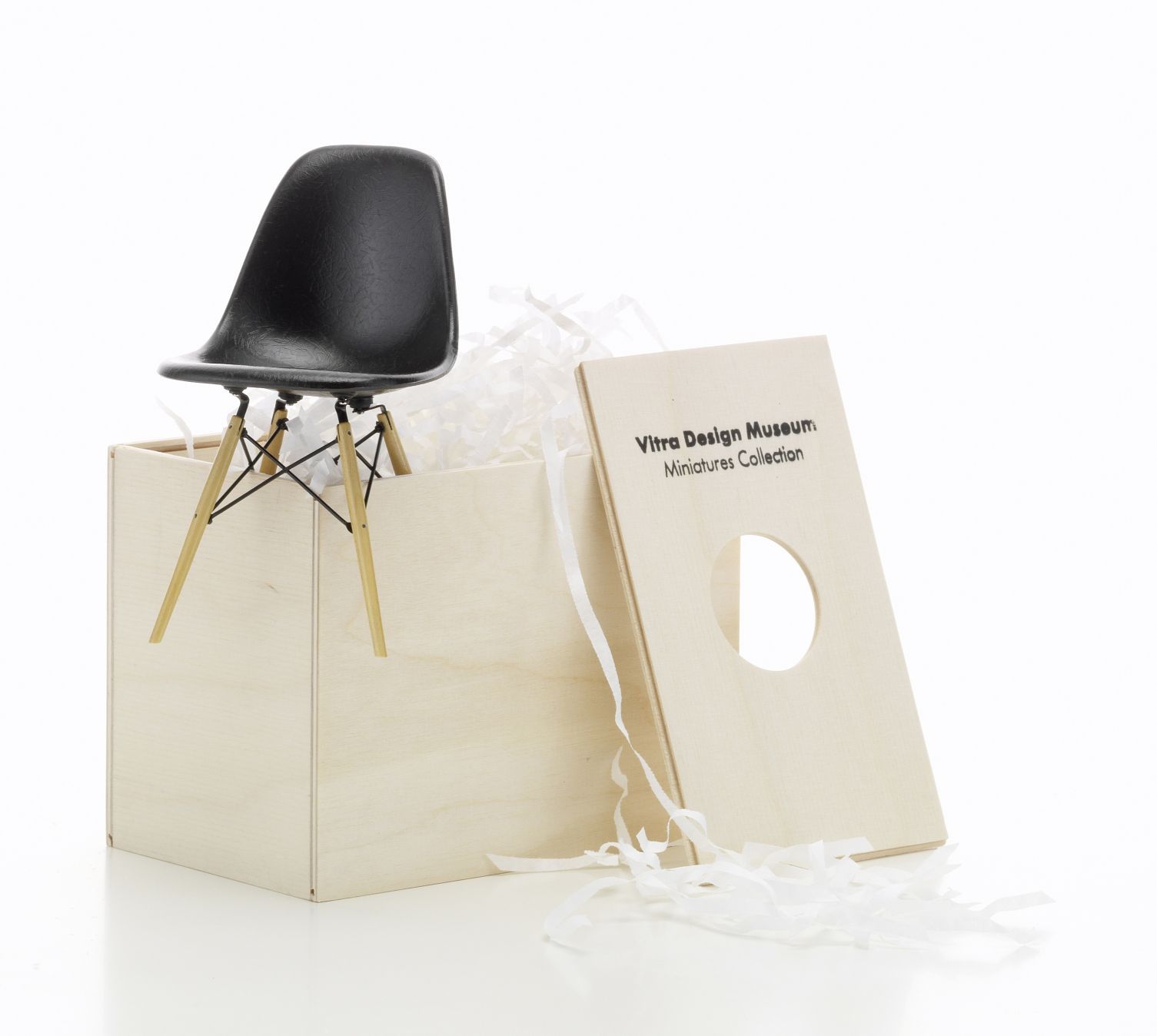 Schwarzer DSW Miniatur Stuhl von Vitra auf einer Holzkiste mit Verpackungsmaterial. Designklassiker Möbel.