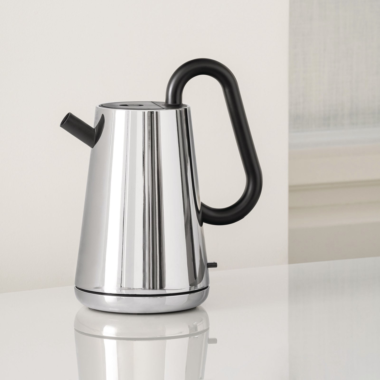 Alessi NE01 B Toru Wasserkocher aus poliertem Edelstahl mit schwarzem Griff auf weißer Oberfläche.