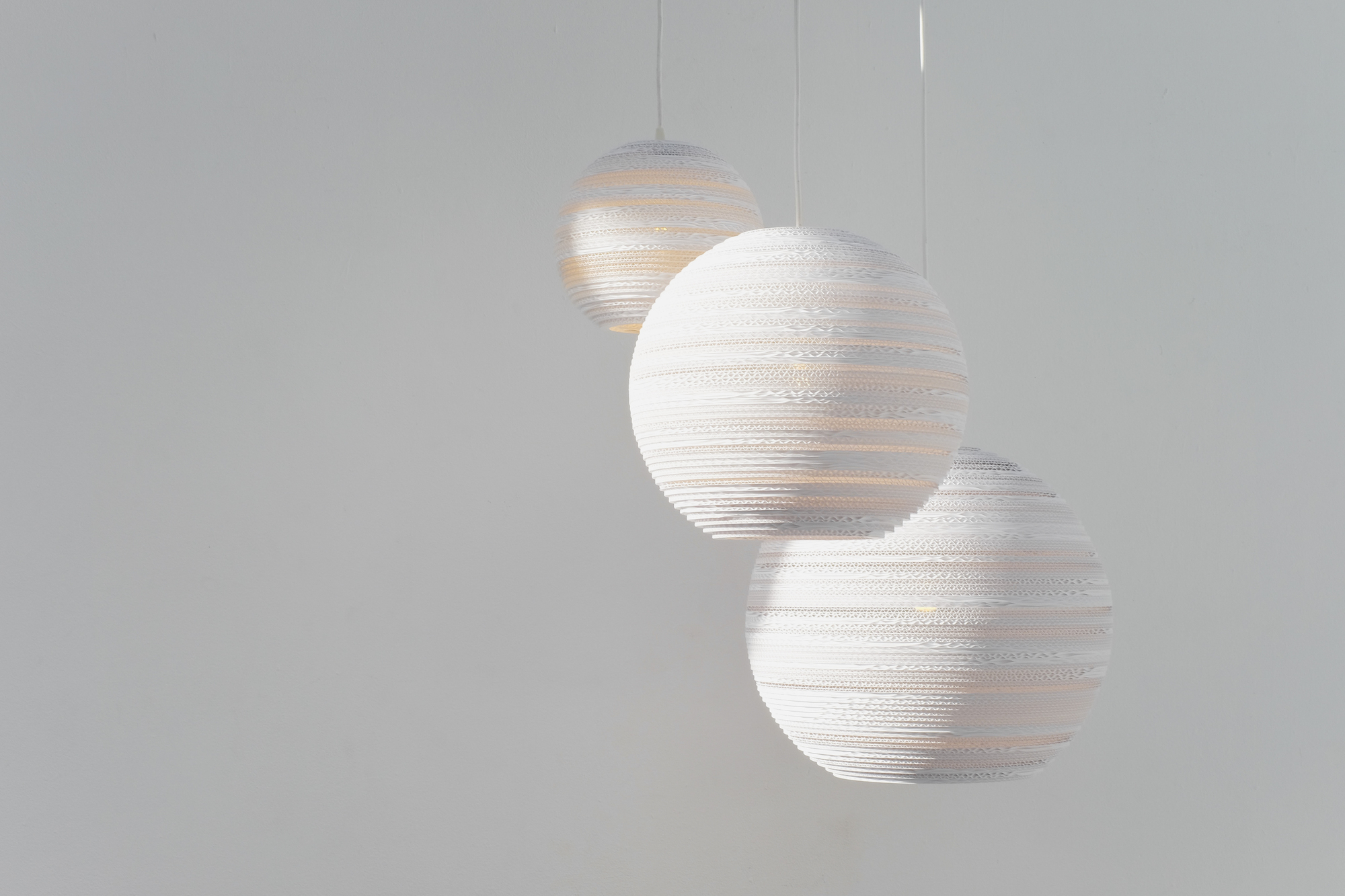 Drei weiße Scraplights Moon Hängeleuchten von Graypants, gefertigt aus recycelter Pappe, für stimmungsvolle Beleuchtung.