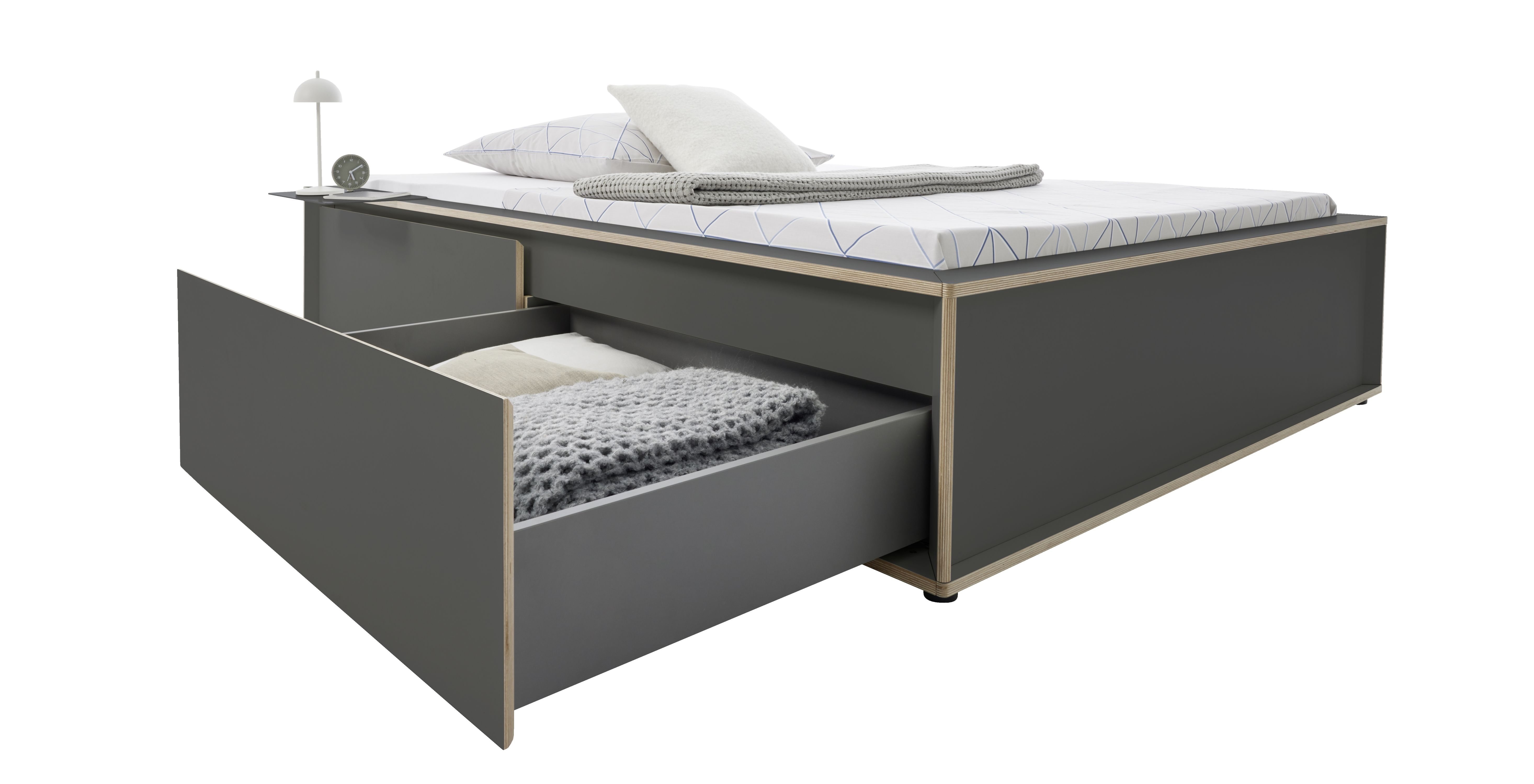 Spaze Bett von Müller Möbelwerkstätten in Grau mit Schublade, Bettwäsche, Lampe und Wecker.