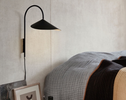 Schwarze Wandleuchte mit konischem Lampenschirm neben einem Bett im Schlafzimmer. Moderne Innenbeleuchtung für Zuhause.