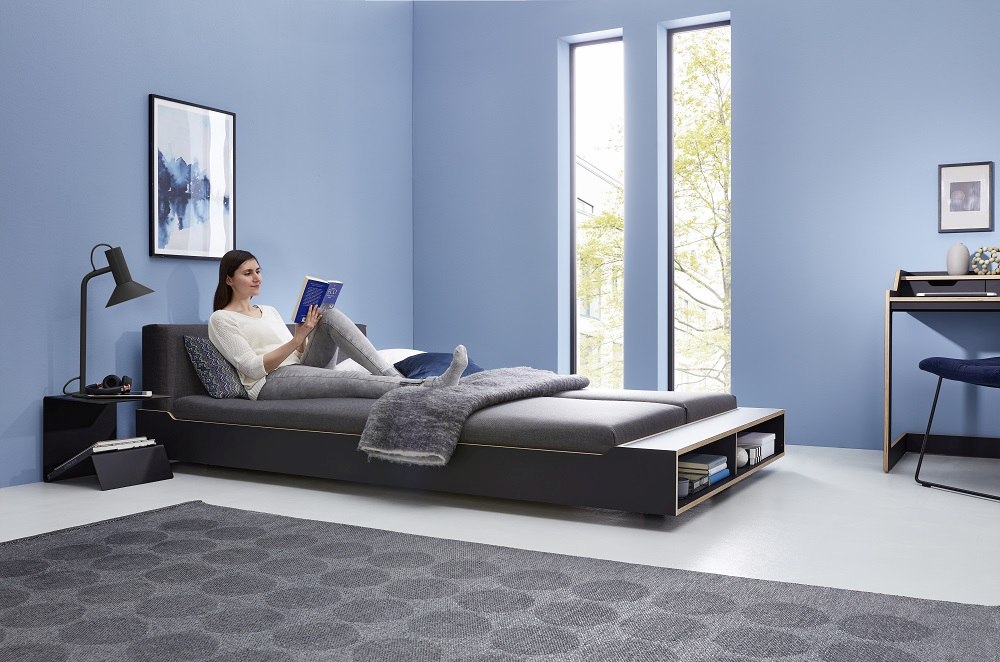 Maude Bett von Müller Möbelwerkstätten in modernem Schlafzimmer mit Frau, Schreibtisch und Teppich.
