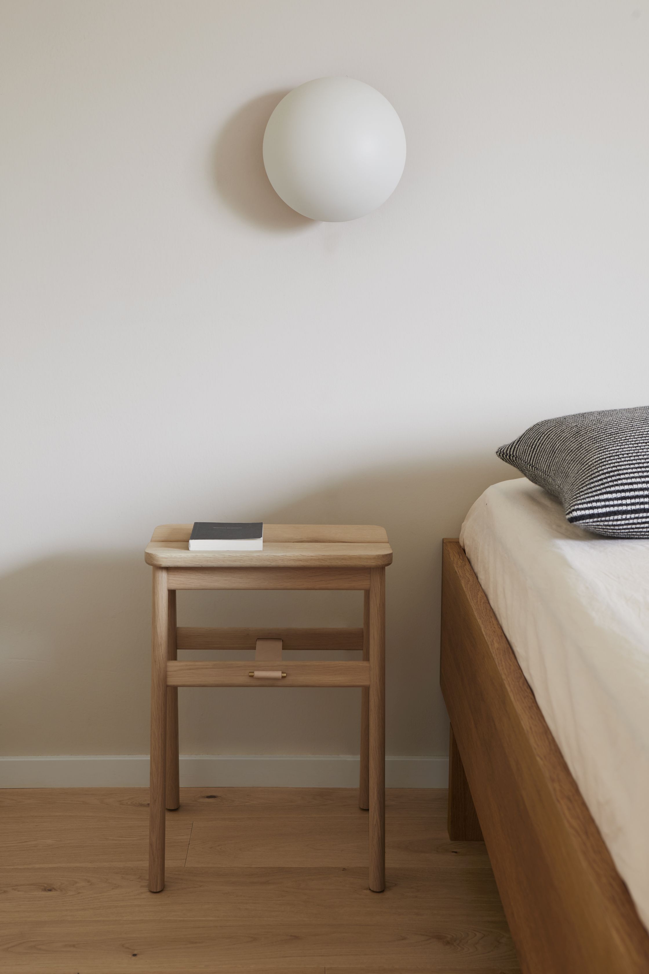 Angle Falthocker Eiche von Form & Refine als Nachttisch im Schlafzimmer mit Buch.
