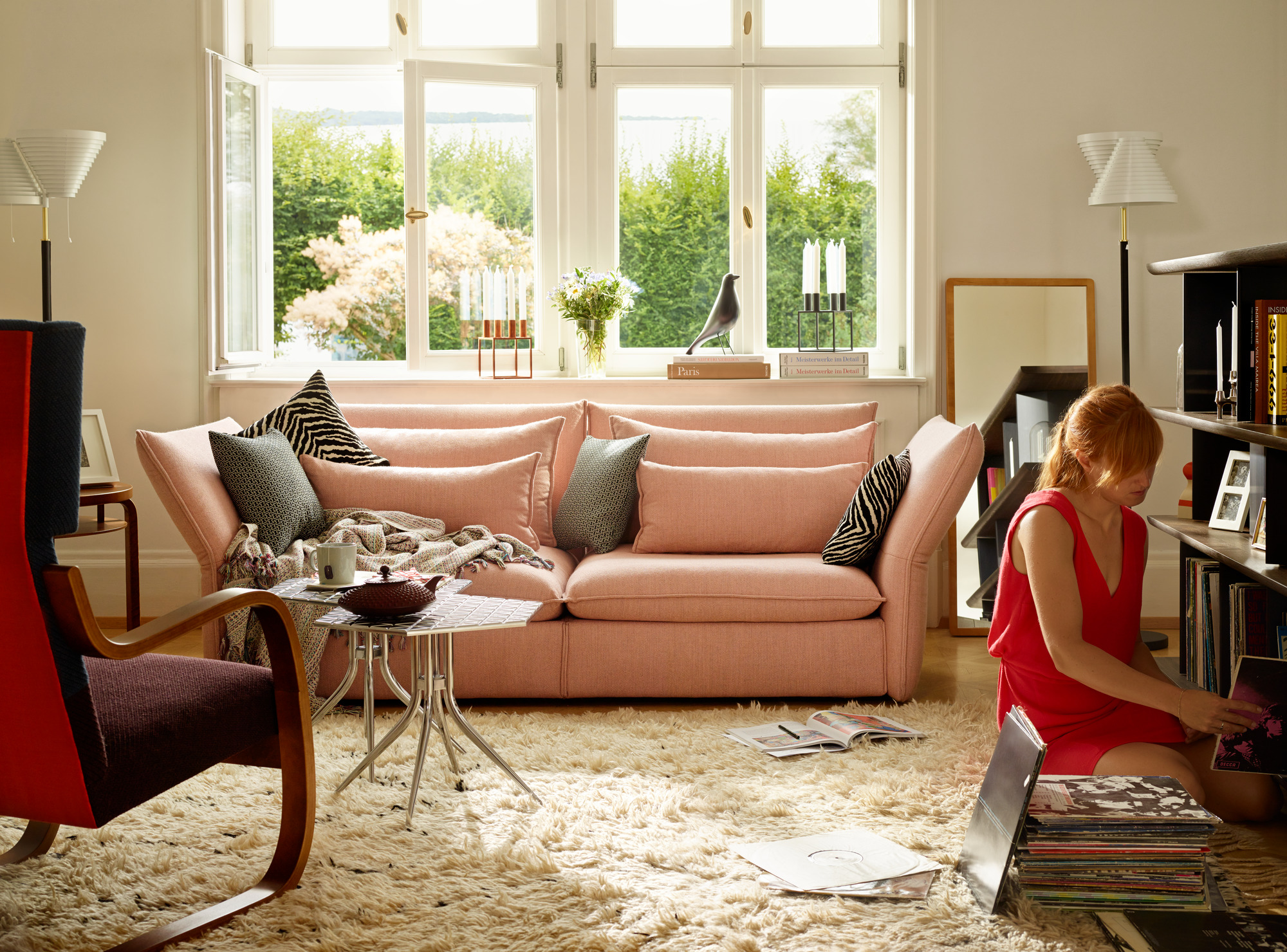 Wohnzimmer mit rosa Mariposa Sofa, Teppich, Frau sucht Schallplatten im Regal.
