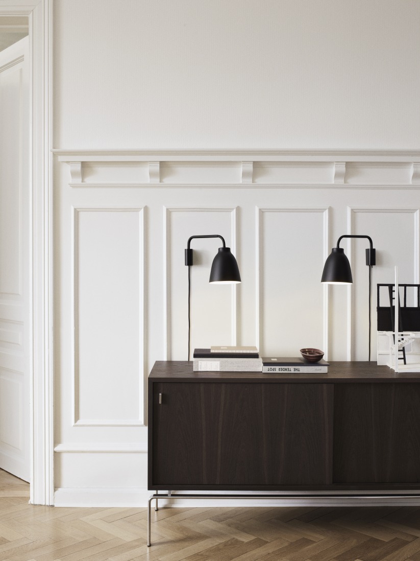 Zwei schwarze Caravaggio Read Wandleuchten von Fritz Hansen über einem Sideboard. Designleuchte für Wohnraum.