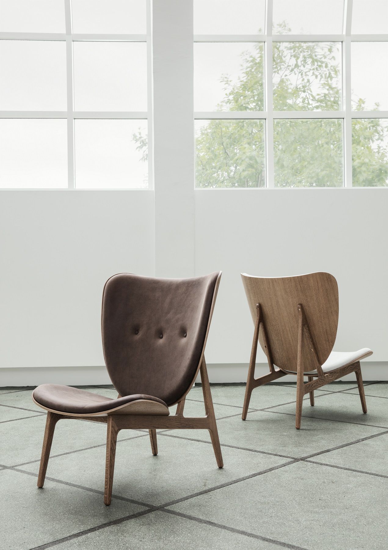 Zwei Elephant Lounge Chairs von NORR11, einer mit braunem Leder, der andere mit hellem Holz.