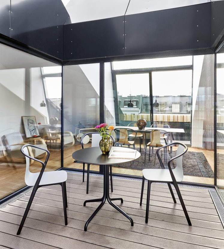 Belleville Table von Vitra, runder Esstisch mit schwarzem Gestell und passenden Stühlen auf einer Terrasse.