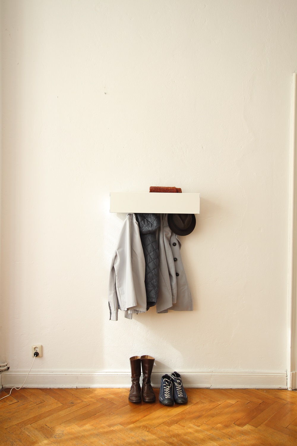 Weiße Wandgarderobe CR Linea1 von Müller Möbelwerkstätten mit Jacken, Schal, Hut und Schuhen im Flur.