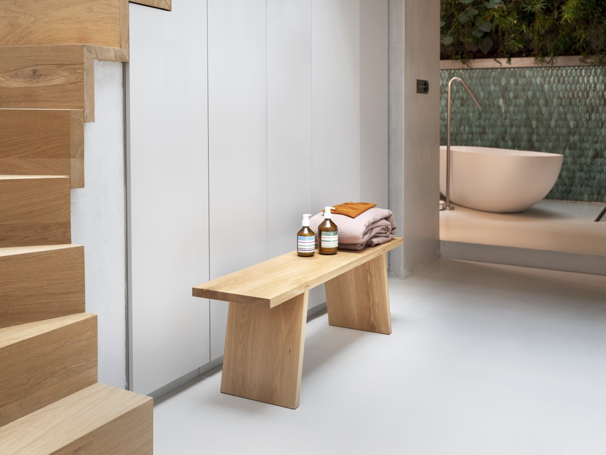 Helle Holzbank "Dovetail Bench" mit Handtüchern und Pflegeprodukten im modernen Badezimmer.