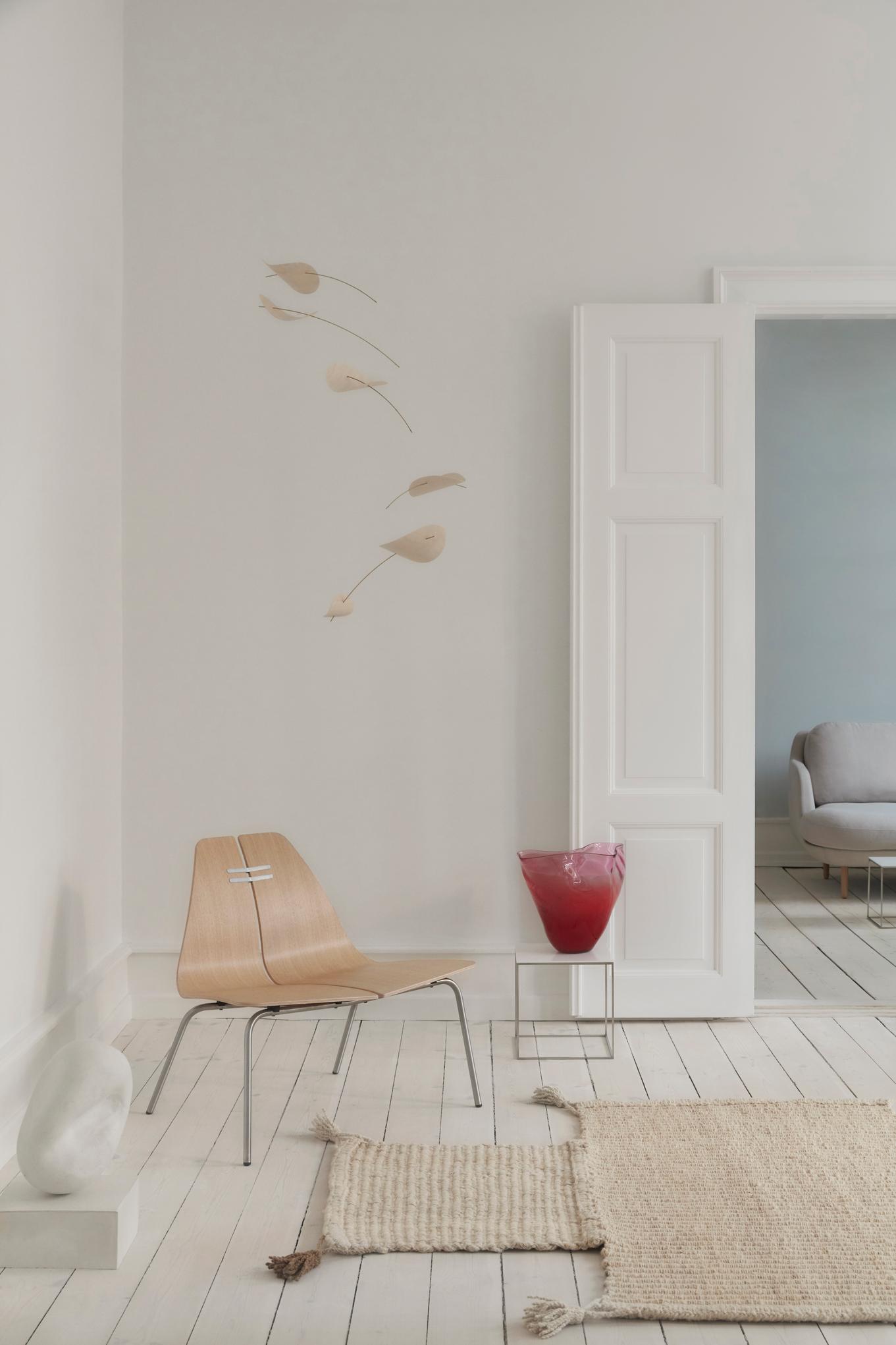 Heller Raum mit PK23 Loungesessel von Fritz Hansen, Holzboden, Teppich, roter Vase und minimalistischer Dekoration.