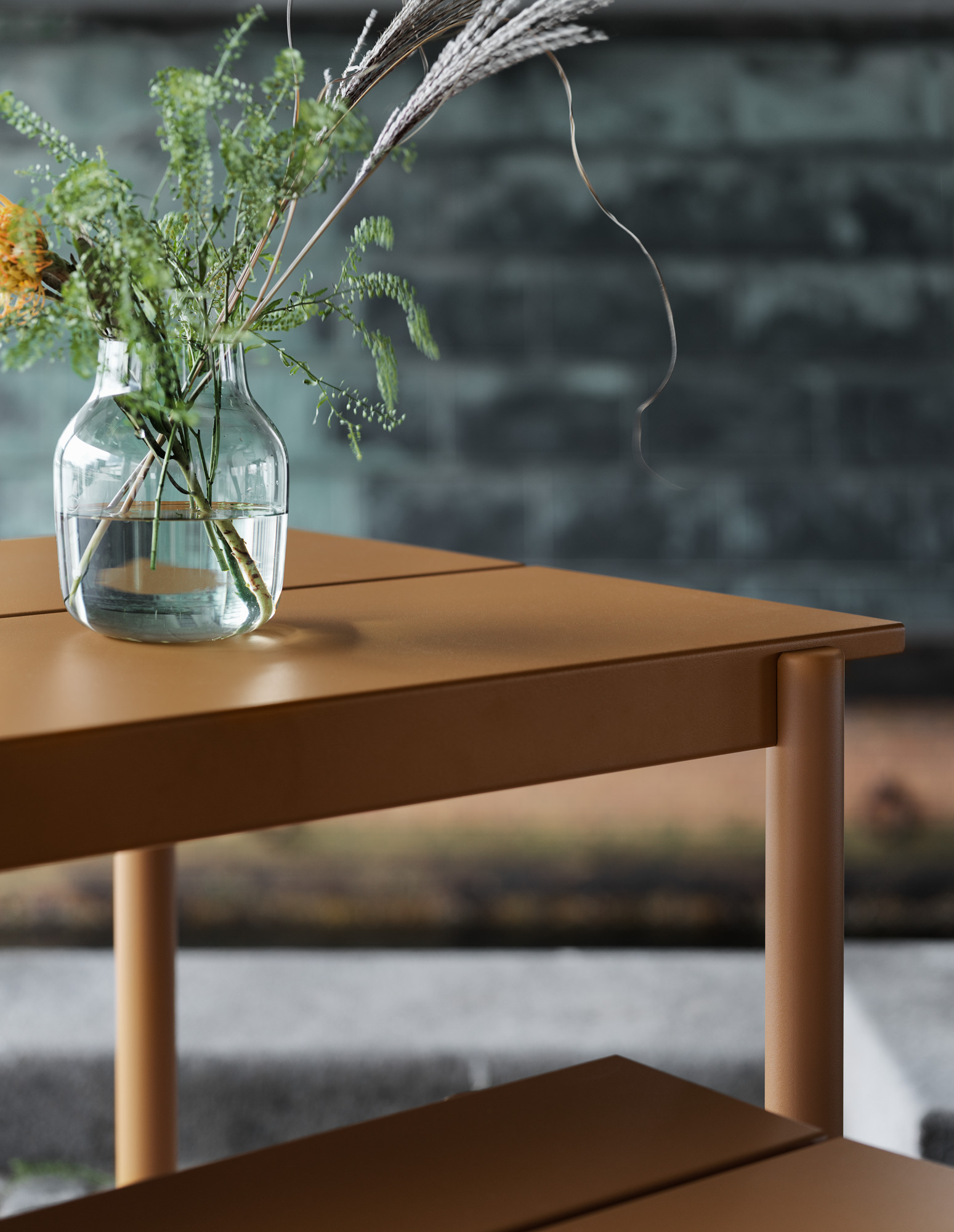 Nahaufnahme des Muuto Linear Steel Outdoor Tisches mit Blumenvase. Gartentisch aus Stahl in Braun.